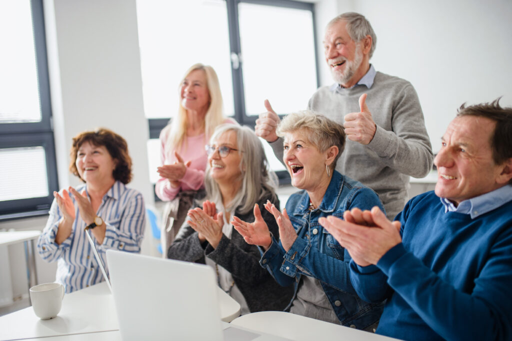 Group of cheerful seniors attending computer and technology education class, laughing and clapping.